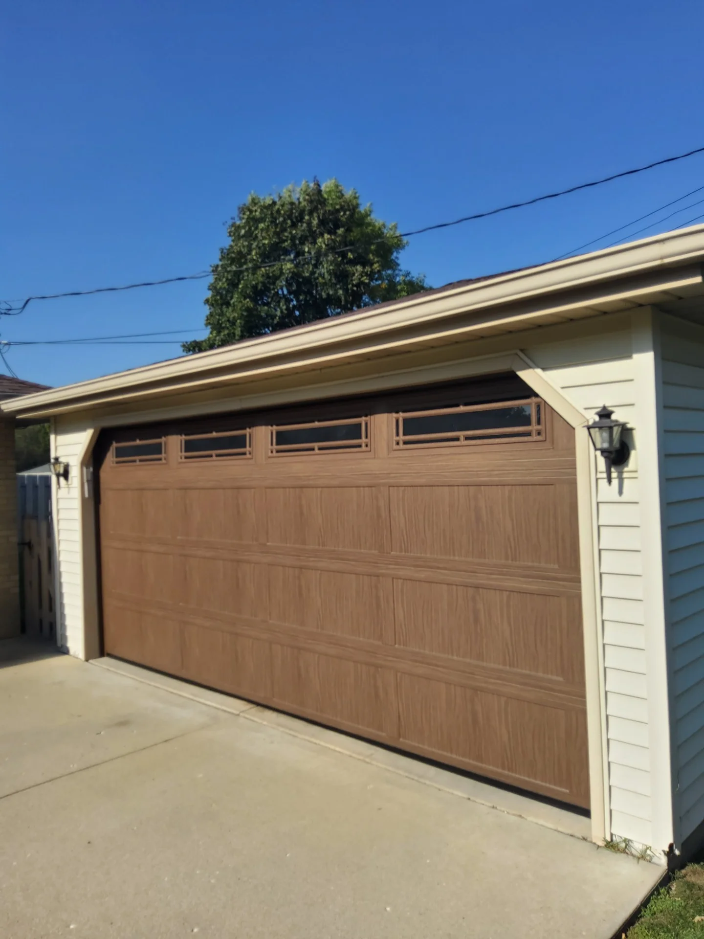 A closed wood-grain sectional residential door with upper window inserts showcasing popular Garage Door Designs in Sussex.