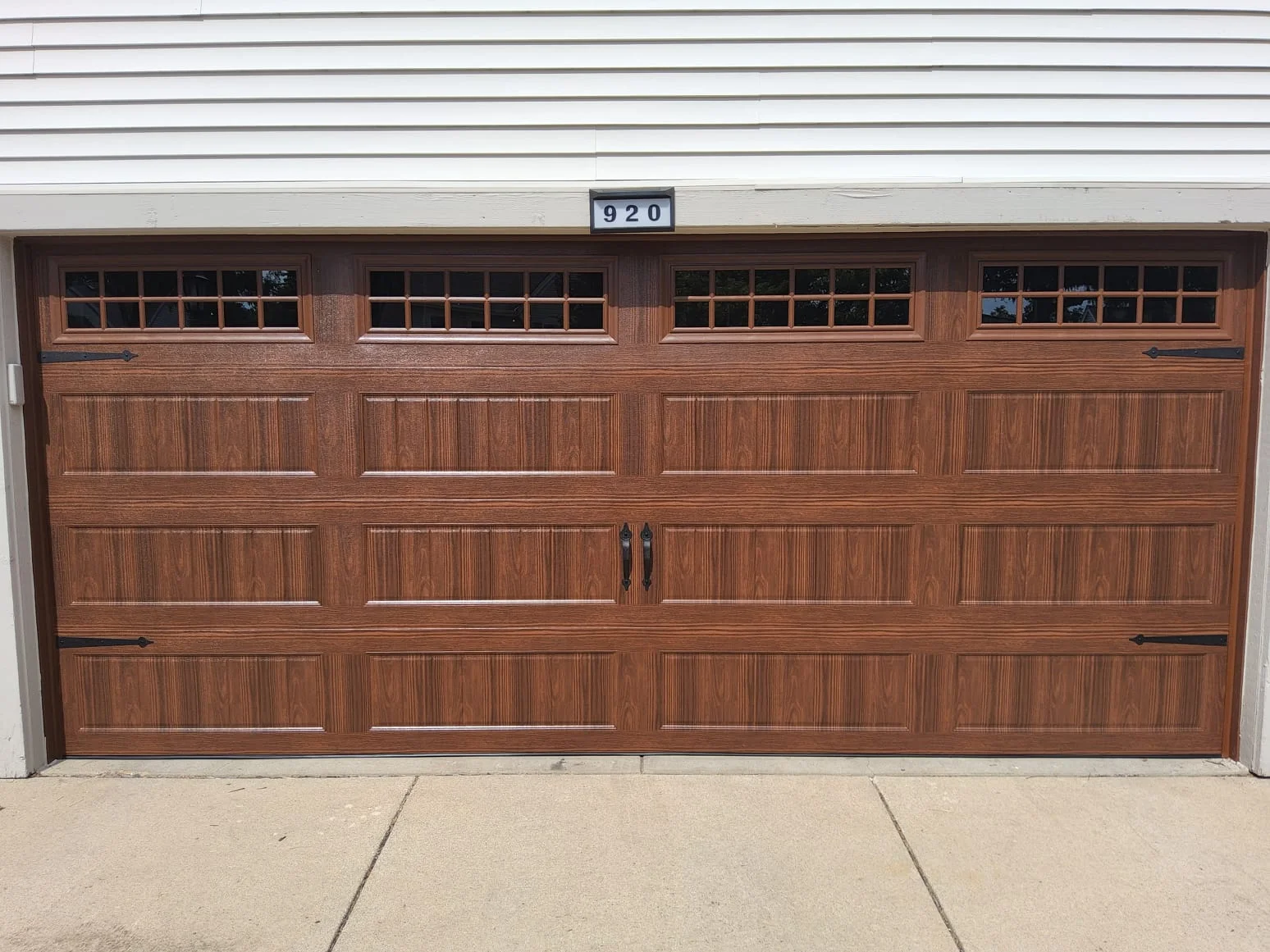 A faux-wood steel sectional door with decorative carriage hardware highlighting an ideal Garage Door Material for Your Home.