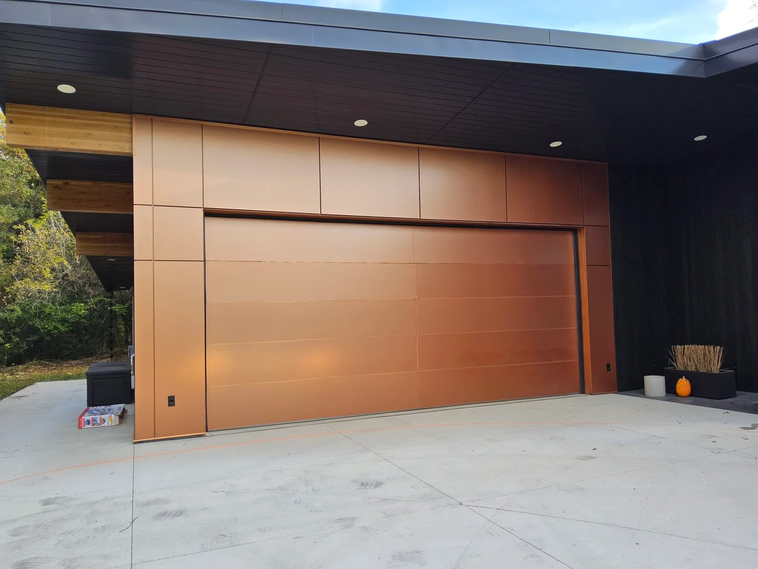 A sleek modern copper-tone flush panel door on a contemporary home demonstrating custom Garage Door Styles in Sussex.