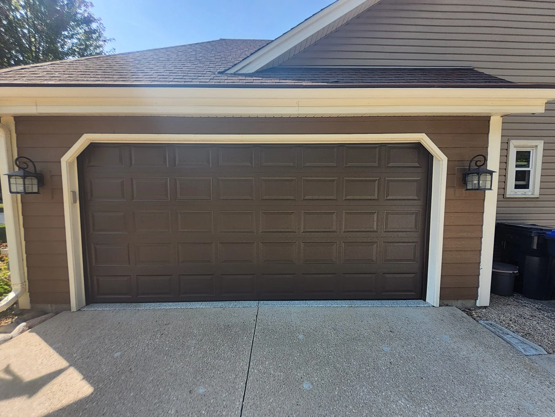 A closed dark brown sectional residential door on a concrete driveway following a Garage Door Repair.
