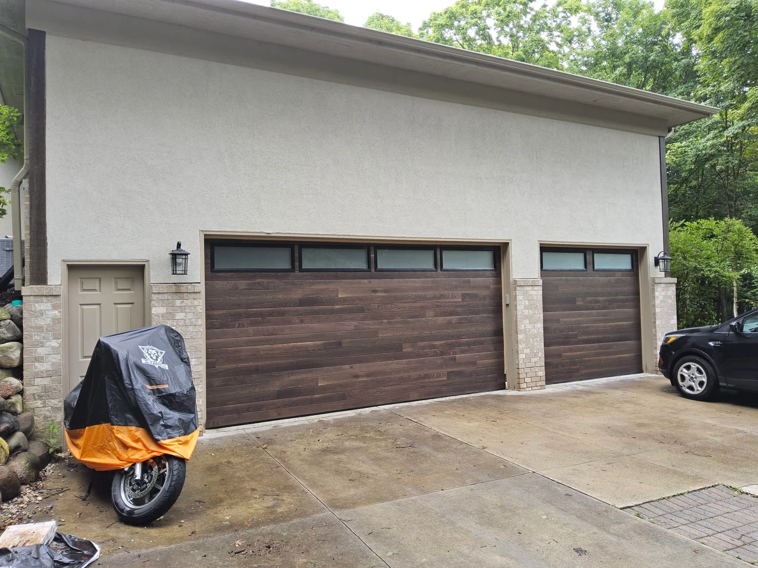 Modern dark wood-look double and single garage doors on a residential home after Garage Door Repair Services.