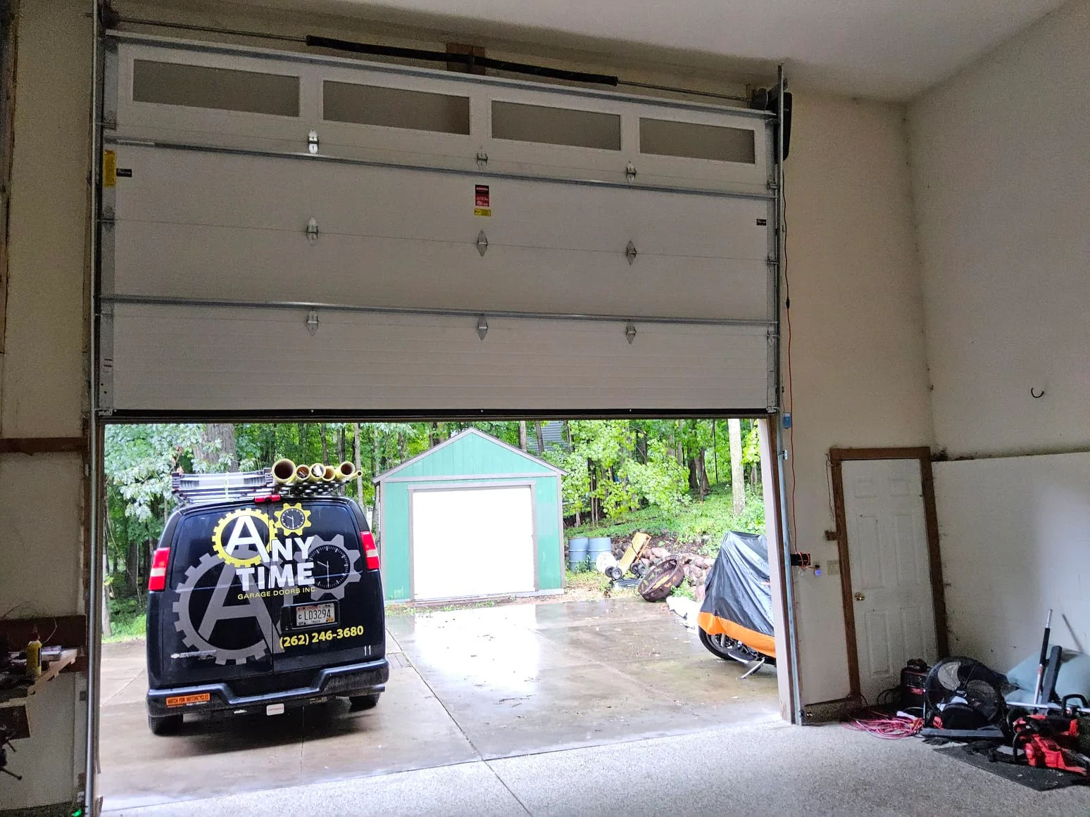 An interior view of a partially raised sectional garage door looks out onto a service van, illustrating a prompt response for urgent garage door spring repair.